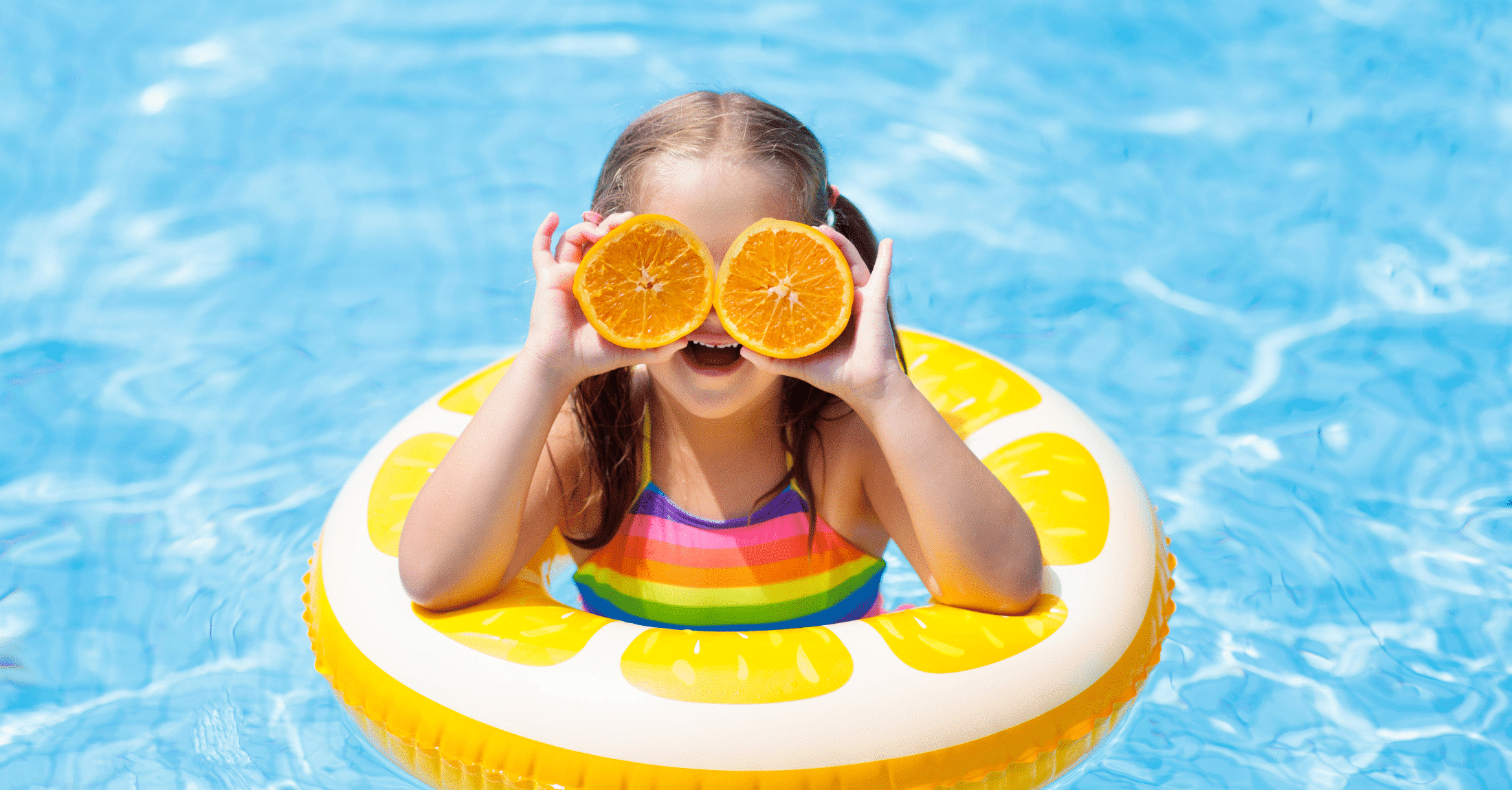 Hymyilevä tyttö uima-altaassa appelsiininpuolikkaat silmälaseina. 